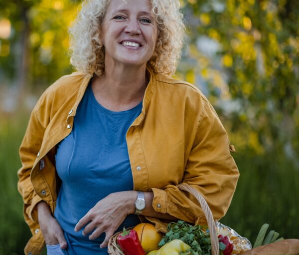 Portrait of mid adult housewife with curly hair standing on the street with hand in pocket, carrying shopping basket and looking at camera